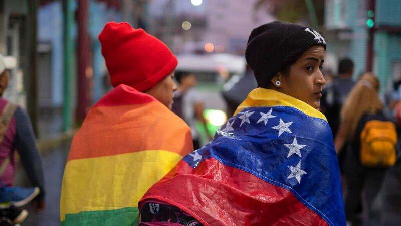 ARCHIVO - Una persona envuelta en una bandera venezolana camina con un grupo de migrantes que...